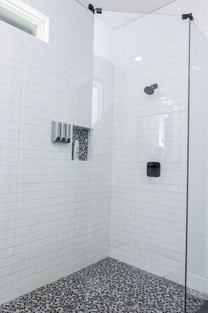 A glass-enclosed shower with white tiled walls and a patterned floor. - Stylish Luxury Downtown Home (Houston)
