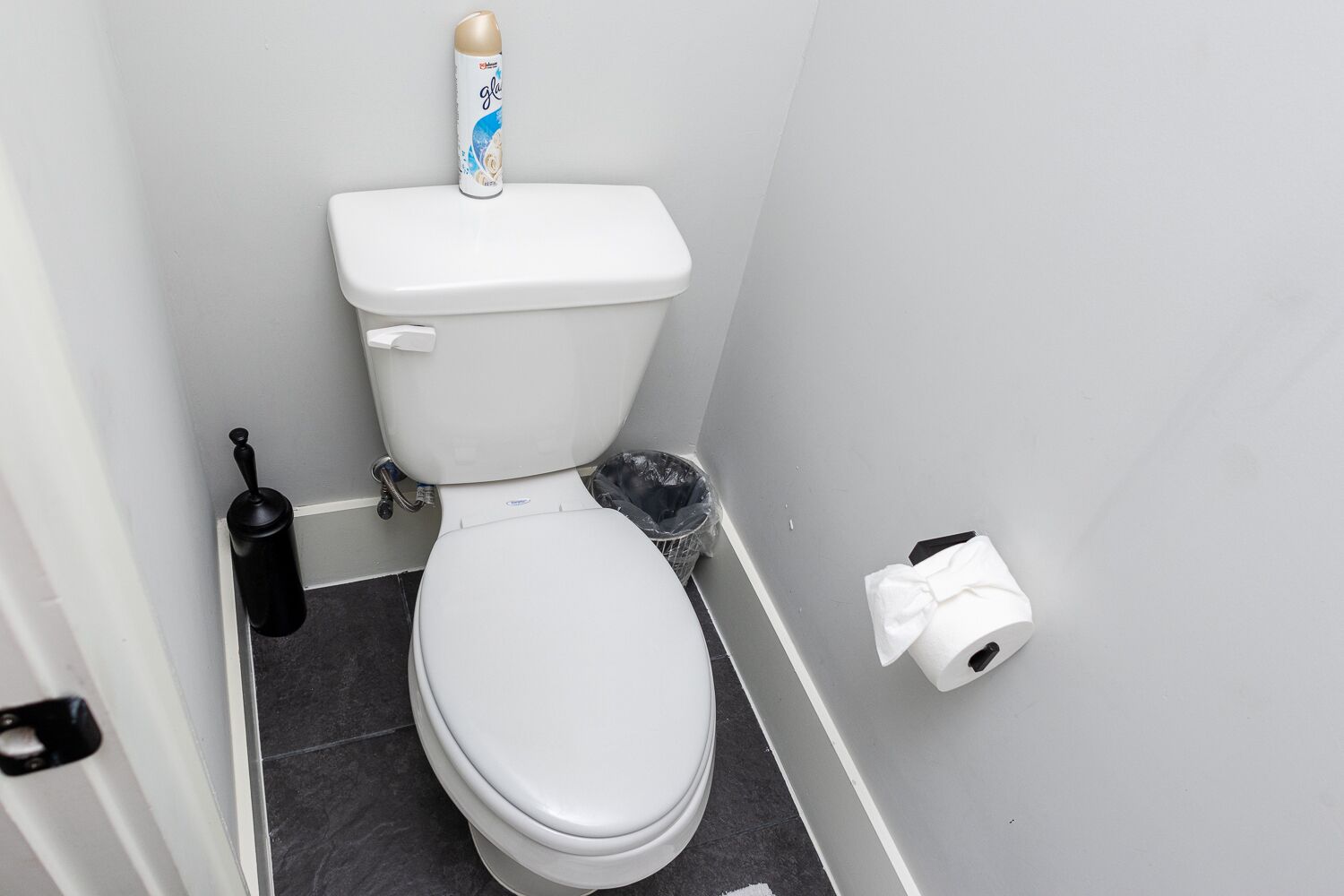 Eine kleine, weiße Toilette mit Papierhalter an der Wand und einem Pömpel auf dem Boden.