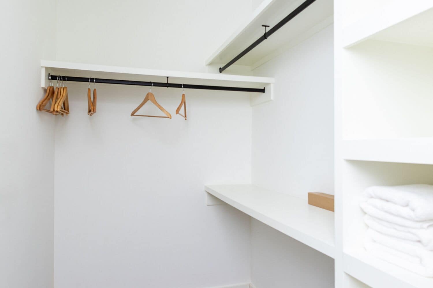 A white closet with wooden hangers and a black rod.