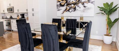 A modern dining area with a glass table and black velvet chairs, white cabinetry, and a large abstract painting.