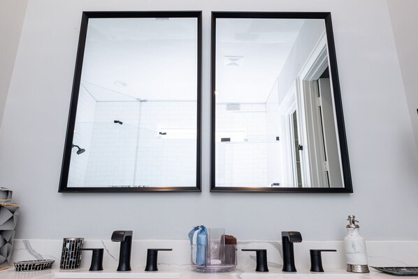 Un baño con dos espejos, un lavabo con grifos modernos, un perchero y un recipiente de vidrio con una esponja.