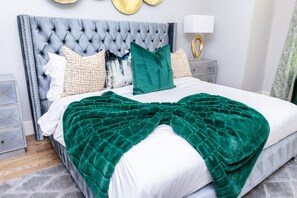 A neatly made bed with a green blanket, a tufted headboard, and patterned pillows. - Stylish Luxury Downtown Home (Houston)