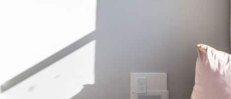 Una habitación moderna con un televisor de pantalla plana grande montado en la pared, una mesita de noche blanca y una almohada rosa.