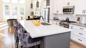 Une cuisine moderne avec des meubles blancs, des appareils en acier inoxydable et un îlot central doté de tabourets de bar.