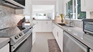 Una cucina moderna con mobili bianchi, forno integrato, piano cottura in acciaio inossidabile, una finestra e un lavello.