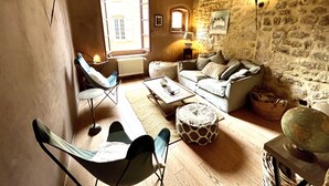 A cozy living room with a stone wall, a sofa, a chair, a coffee table, and a lamp. - Beautiful Townhome in Uzès Center (Uzès)