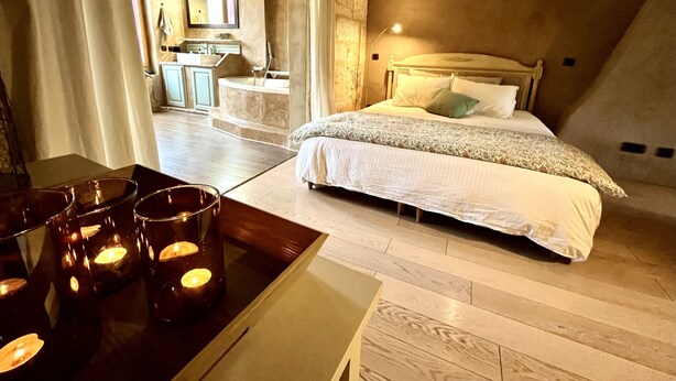 A bedroom with a bed, bedside table, and candles. There is a bathroom with a sink and mirror in the background. - Beautiful Townhome in Uzès Center (Uzès)