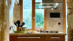 A kitchen with wooden cabinets, a built-in stove, and a window with a view of greenery. - Beautiful Townhome in Uzès Center (Uzès)