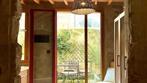 A rustic interior with a wooden ceiling, a woven light fixture, a red door leading to a patio with a table and chairs, and a stone wall. - Beautiful Townhome in Uzès Center (Uzès)