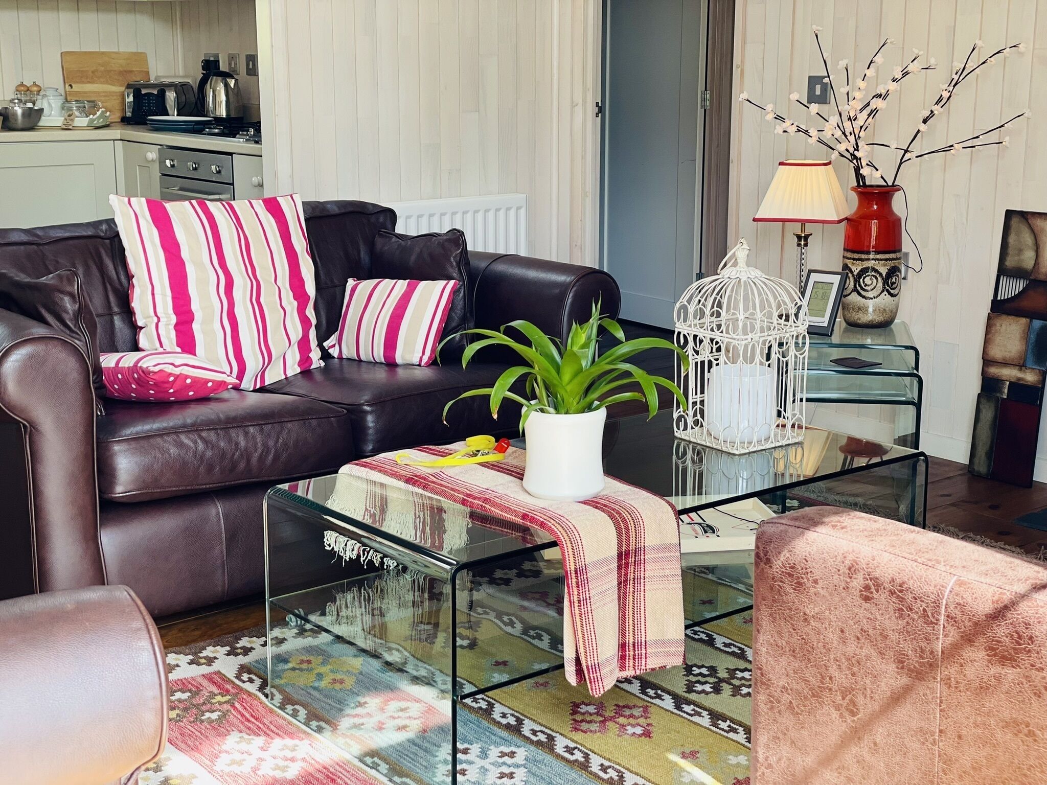 A living room with a leather sofa, a glass coffee table, a potted plant, and a decorative birdcage.
