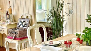 Un coin repas avec une table en bois mise pour le repas, comprenant des assiettes, des verres et un centre de table composé de tomates et de basilic.