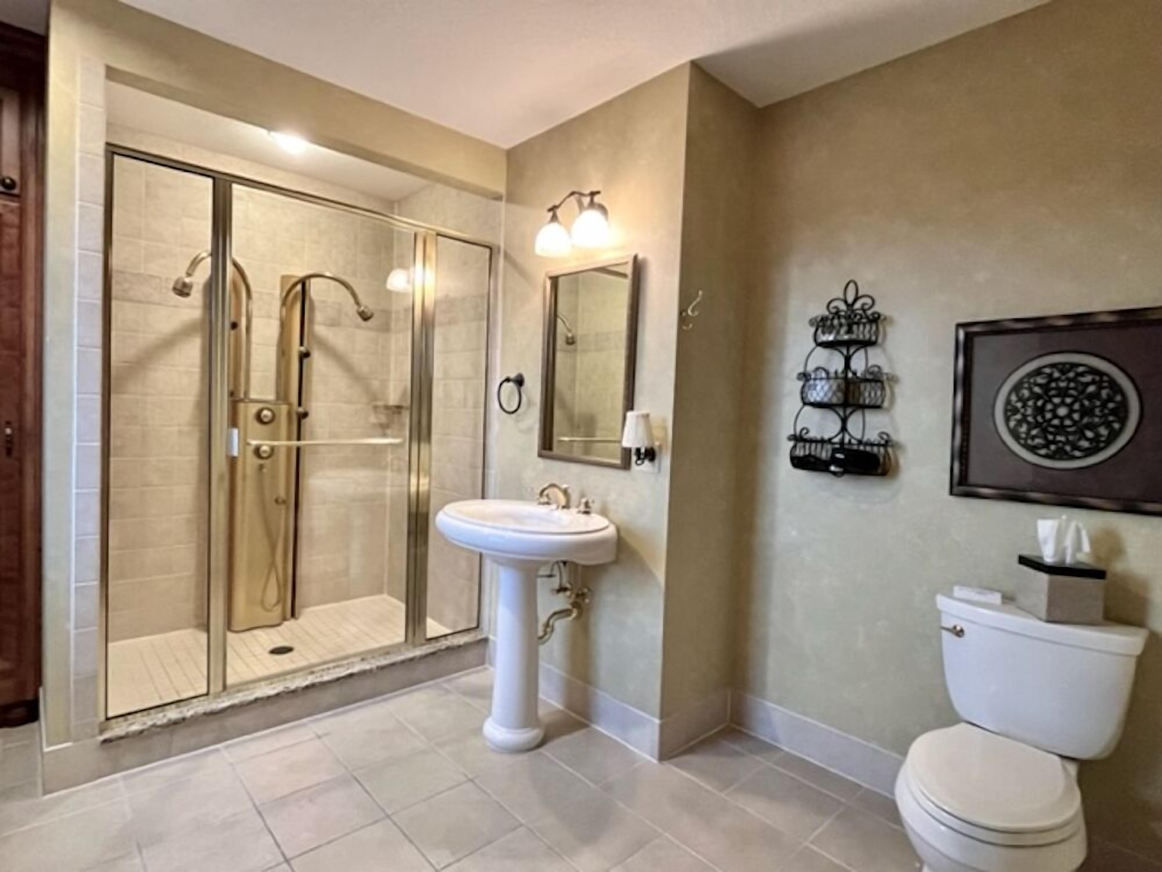 A bathroom with a glass-enclosed shower, a pedestal sink, a toilet, and a wall-mounted mirror.