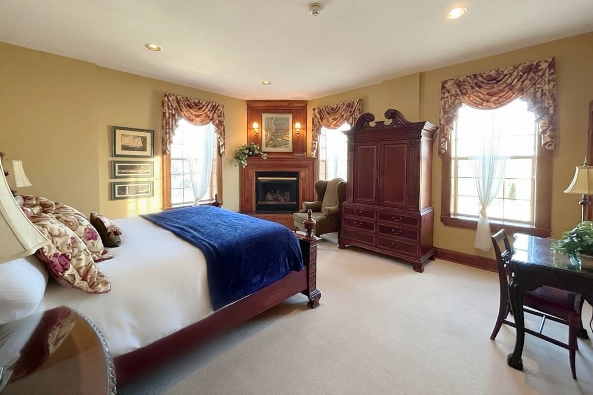 A bedroom with a large bed, a fireplace, a wooden cabinet, and a dining table with chairs.