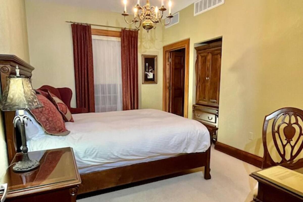 A bedroom with a large bed, a wooden nightstand, a chair, a chandelier, and a wardrobe.