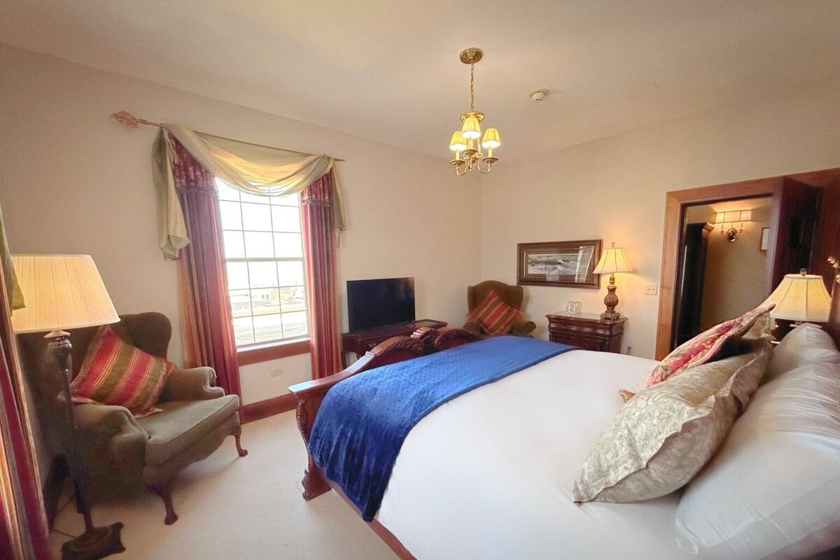 A hotel room with a large bed, a desk, a chair, a television, and a window with curtains.