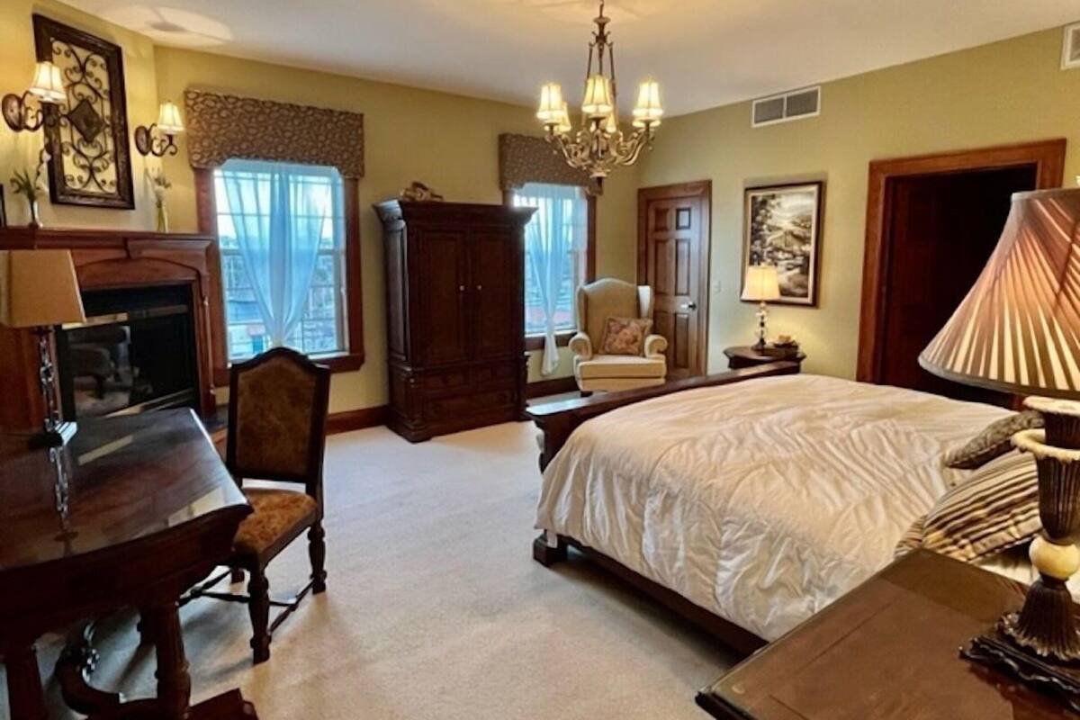 A bedroom with a bed, a desk, a chair, a wardrobe, a chandelier, and a television.