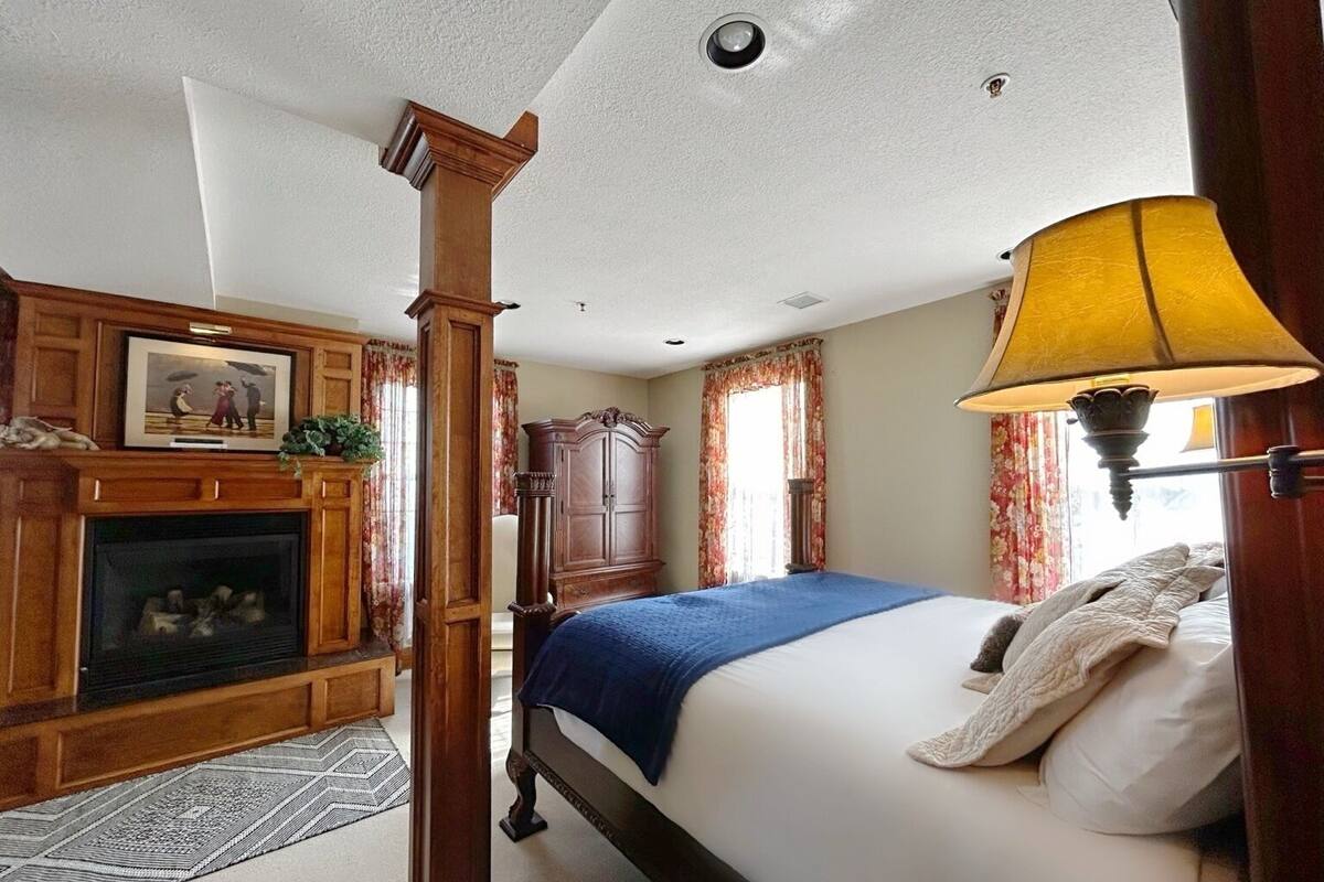 A bedroom with a four-poster bed, a fireplace, and a lamp.