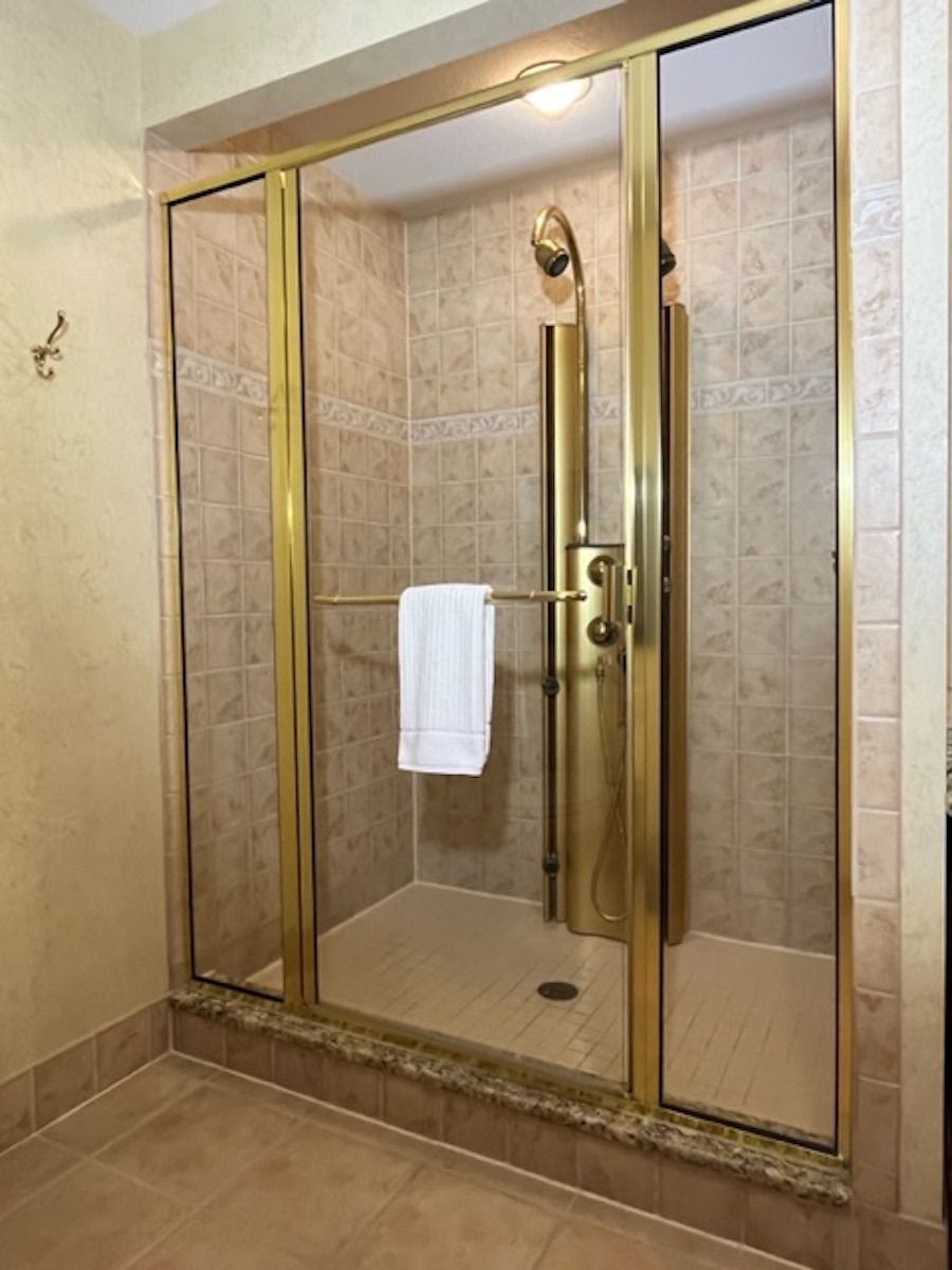 Ducha a pie con mampara de vidrio, una toalla colgada en la puerta y paredes de azulejos.