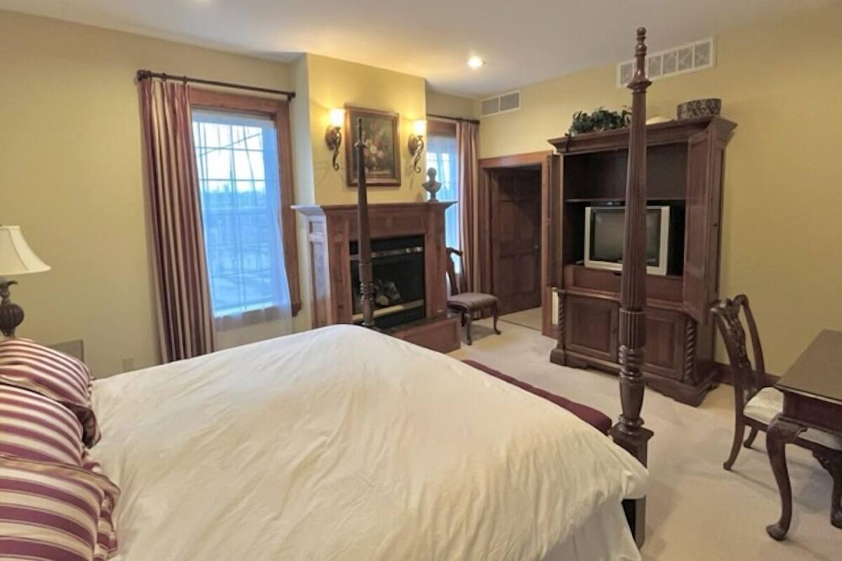 A bedroom with a large bed, a television, a fireplace, and a window with curtains.