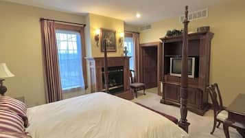 A bedroom with a large bed, a television, a fireplace, and a window with curtains.
