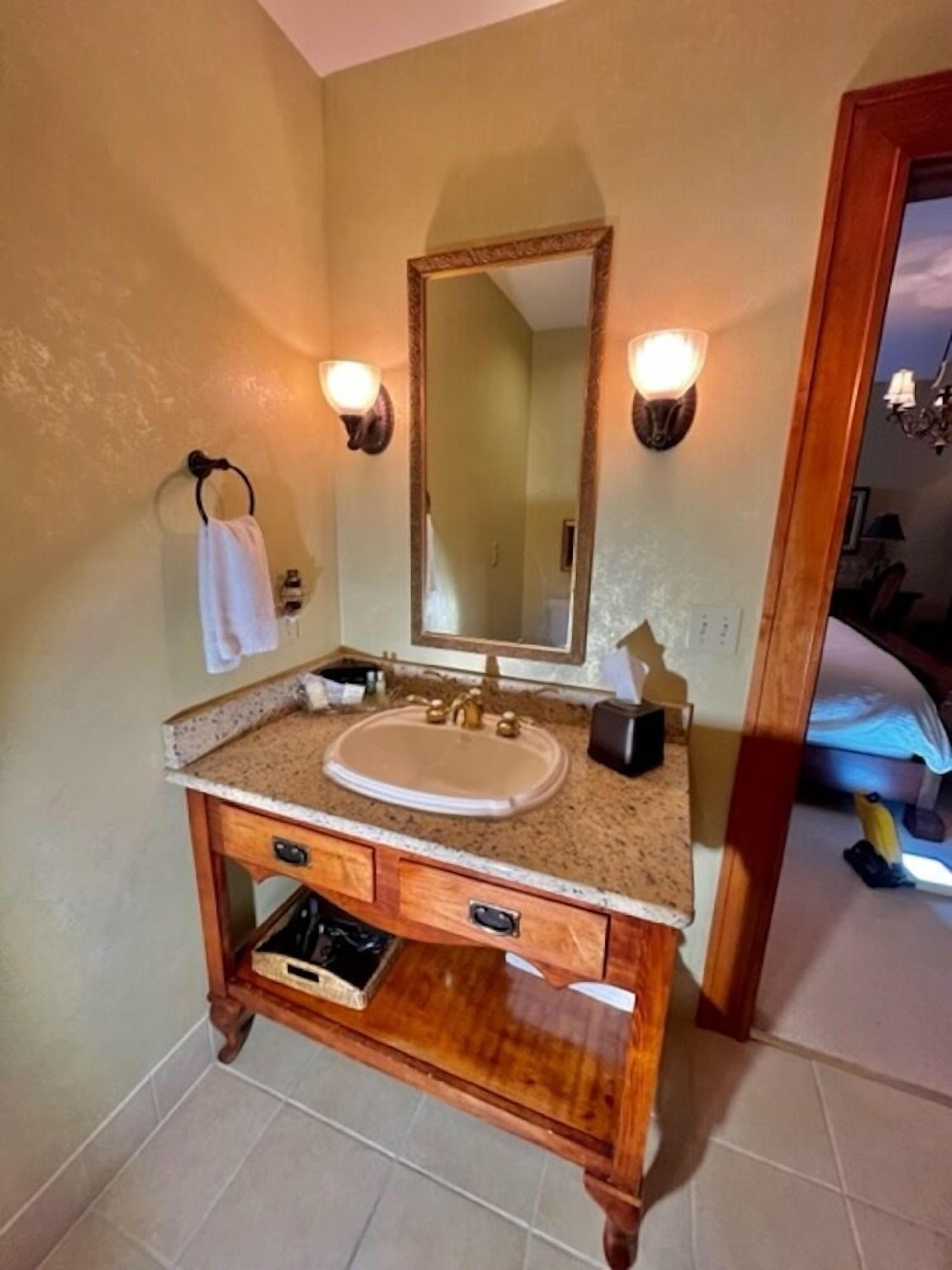 A bathroom with a wooden vanity, a large mirror, and two wall-mounted lights.