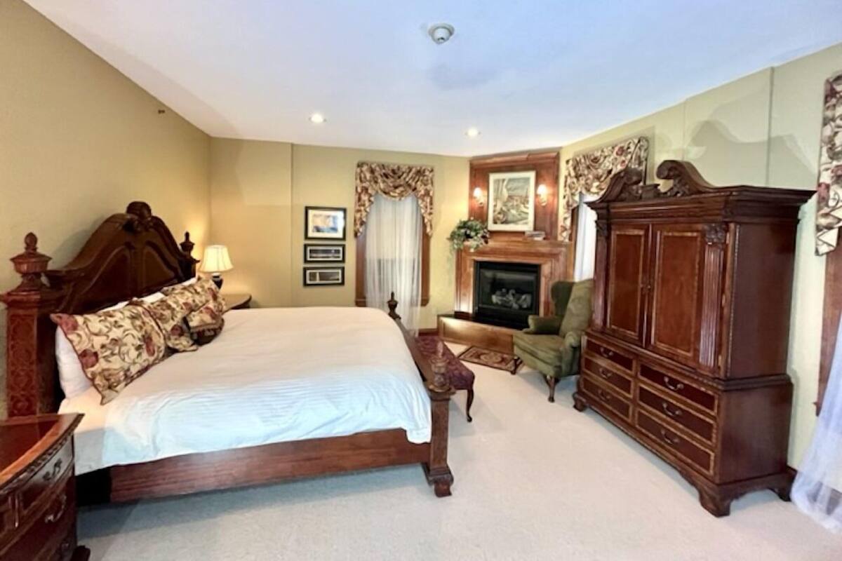 A bedroom with a large bed, a dresser, a fireplace, and a mirror.