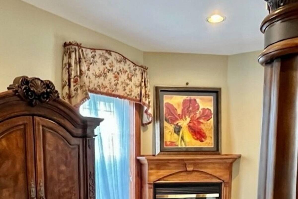 A room with a wooden cabinet, a green armchair, a fireplace, and a framed floral painting on the wall.