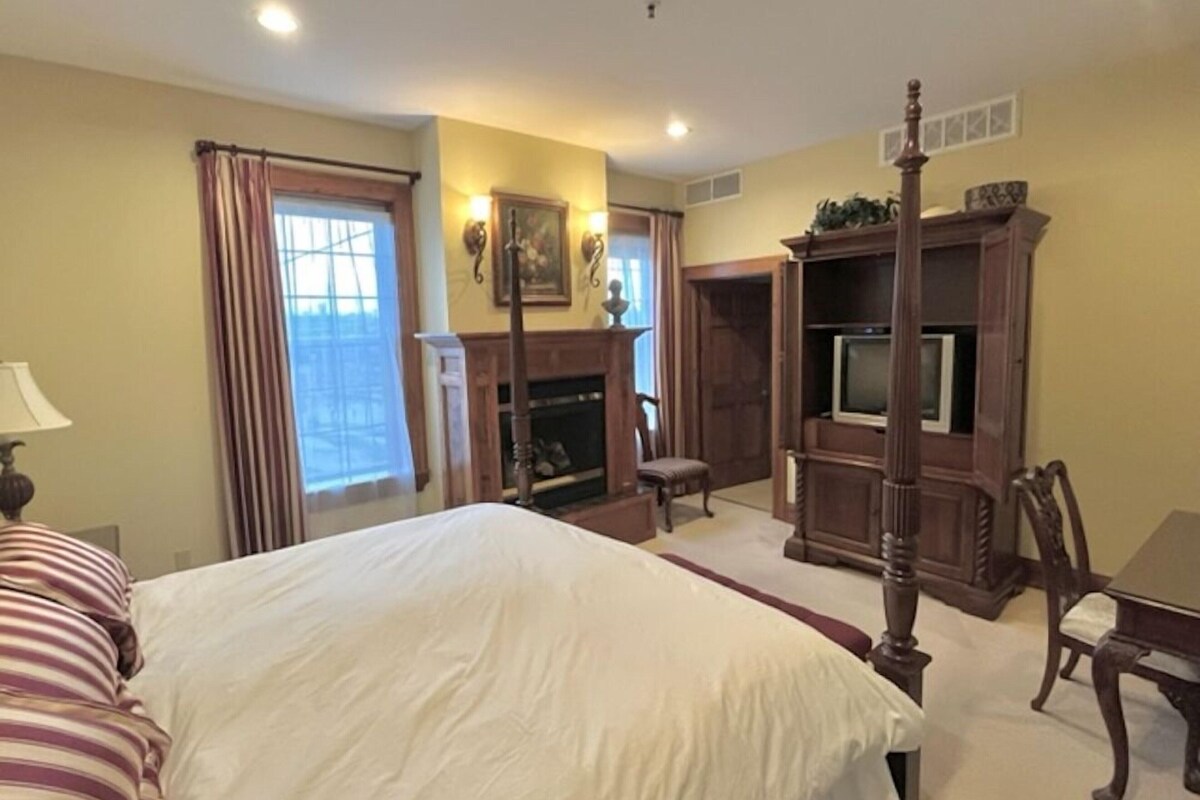 A bedroom with a large bed, a fireplace, a television, and a dining table.
