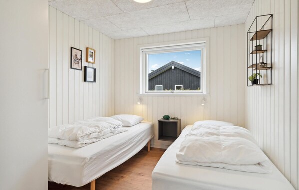 A bedroom with two single beds, a window with a view of a building, and a shelf with plants.