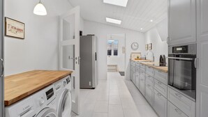A modern kitchen with a Bosch washing machine, a refrigerator, a sink, and a clock on the wall.