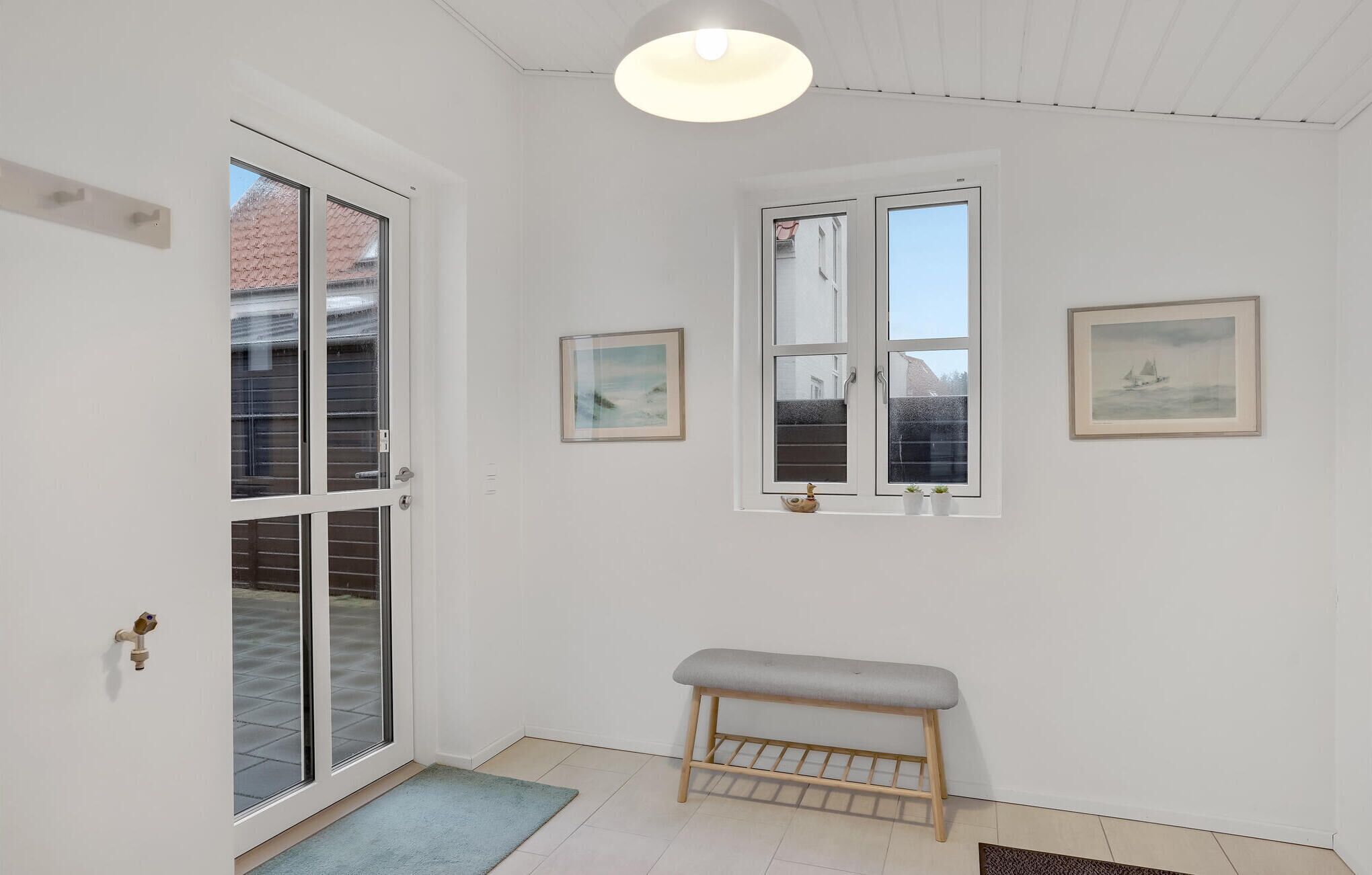 Une pièce comprenant un banc, une porte avec des panneaux de verre, une fenêtre donnant sur un paysage agréable et deux tableaux encadrés accrochés au mur.