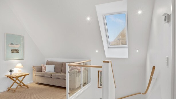 A modern loft bedroom with a sloped ceiling, a loft bed, a small table with a lamp, and a framed picture on the wall.