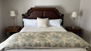 Uma cama bem arrumada com colcha estampada, duas luminárias de cabeceira e uma cabeceira de madeira.