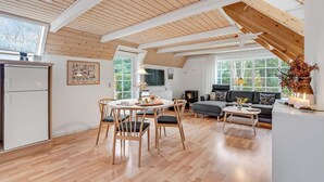 A spacious living area with a high ceiling, wooden beams, a dining table with chairs, a sofa, and a fireplace.