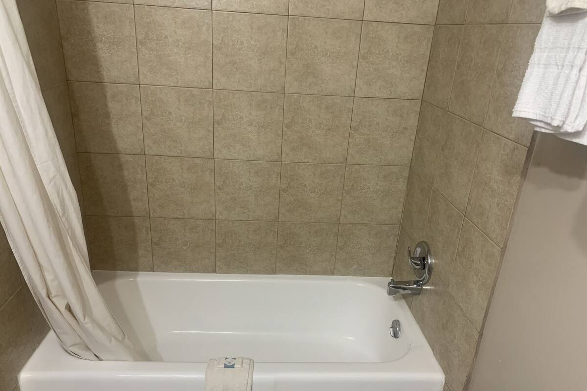 A bathroom with a white bathtub, beige tiled walls, and a white towel hanging on the wall.