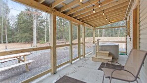 A covered outdoor area with wooden beams, large windows, a hot tub, and a picnic table. - Jim Thorpe Rustic Cabin With Hot Tub, EV Charger, BBQ Grill & Outdoor Games! (Jim Thorpe)