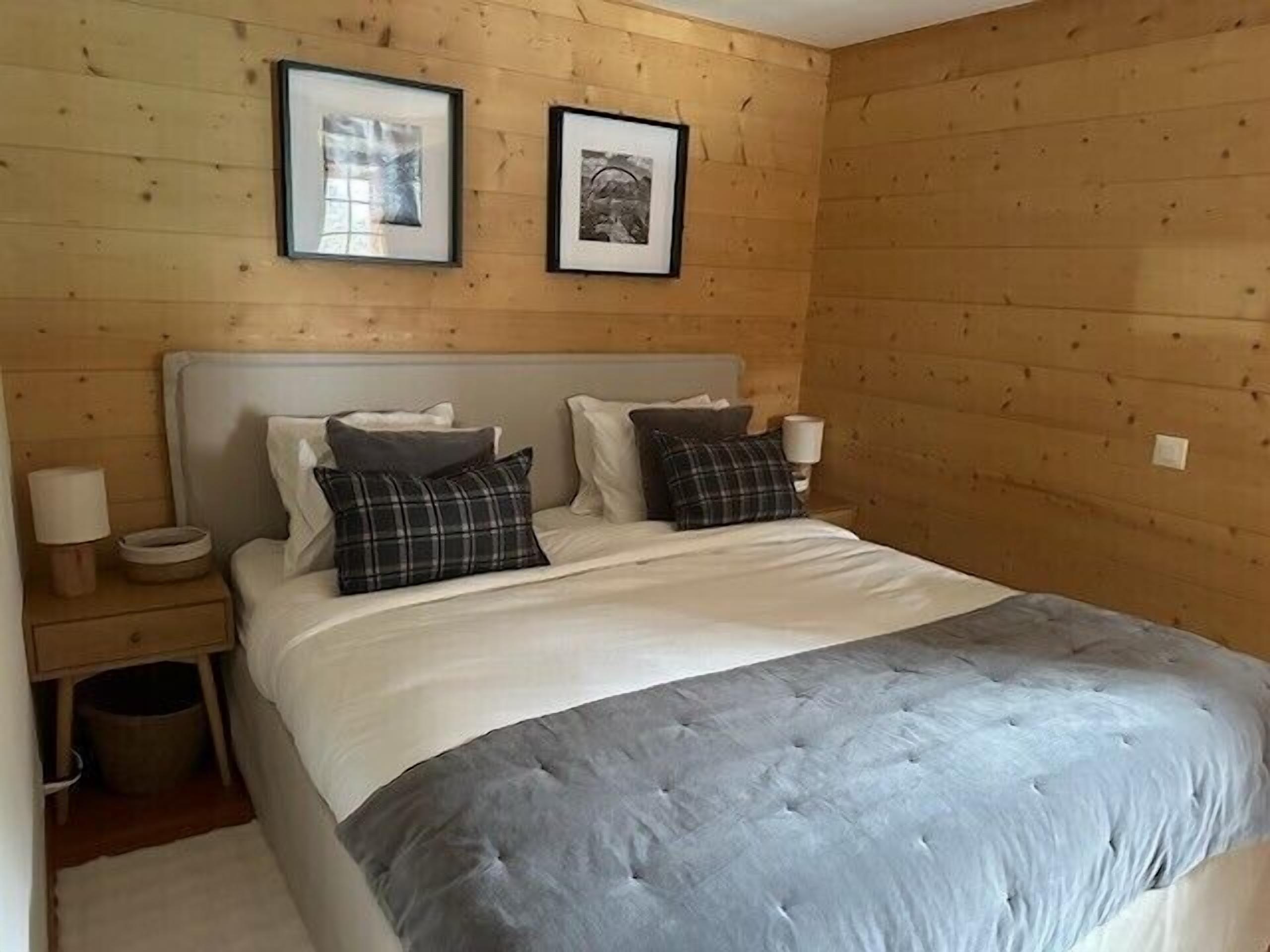 A wooden-paneled bedroom with a bed, two framed pictures, a nightstand, and a lamp.