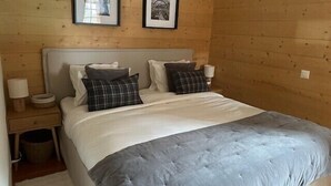 Un dormitorio con paneles de madera, una cama, dos cuadros enmarcados, una mesita de noche y una lámpara.