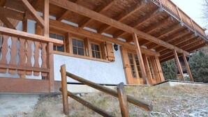 Una cabaña de madera con balcón, ventanas amplias y base de piedra.