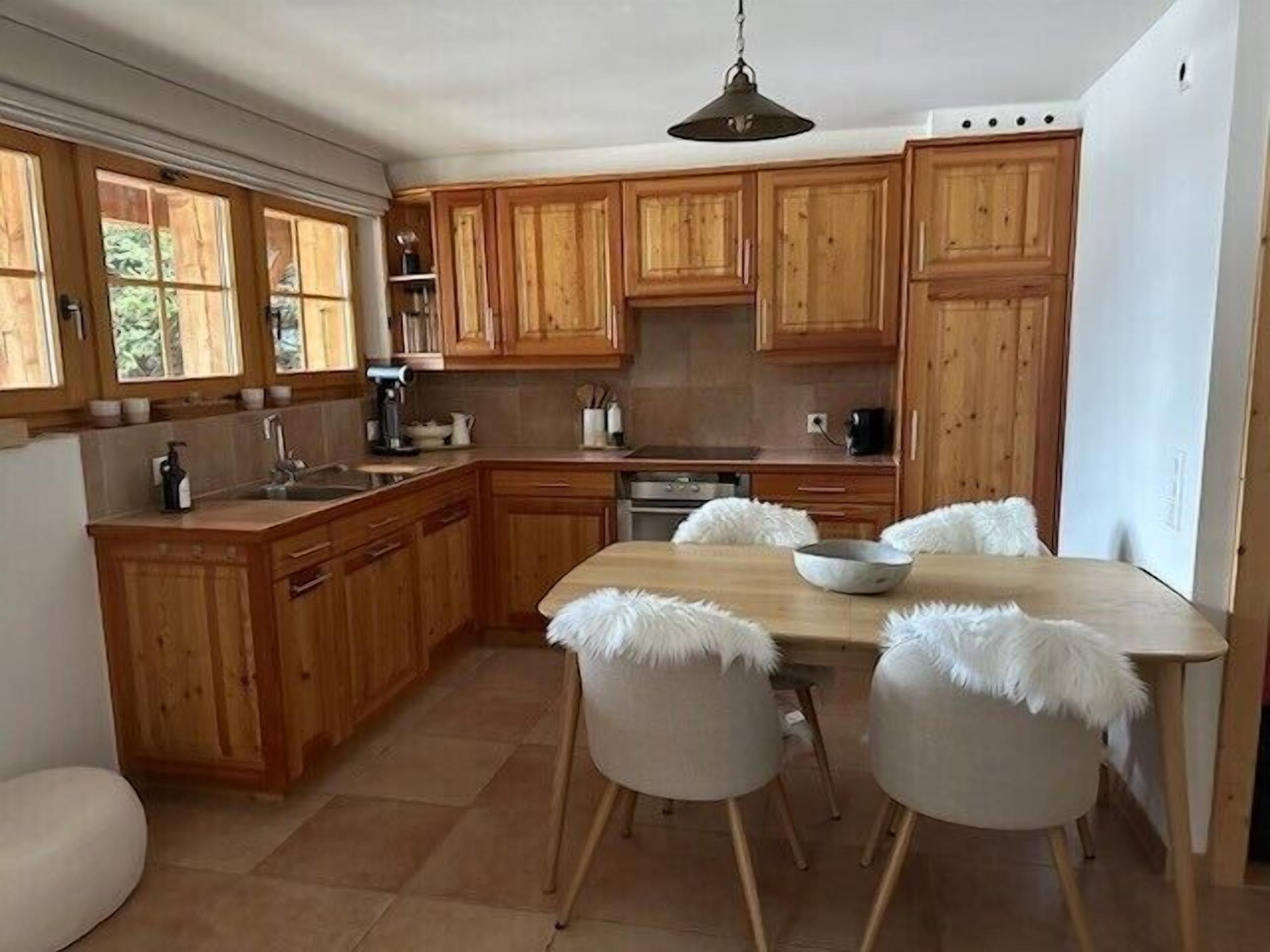 A kitchen with wooden cabinets, a dining table with chairs, and a hanging light fixture.