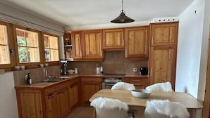 Una cocina con armarios de madera, una mesa de comedor con sillas y una lámpara colgante.