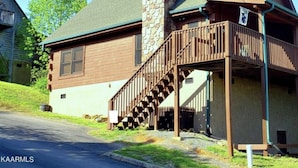 A two-story log cabin with a stone chimney, wooden deck, and a small porch. - SMOKY MOUNTAIN HIGH GETAWAY (Sevierville)