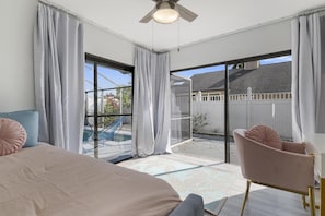 Ein Schlafzimmer mit einem großen Bett, einem Sessel und Blick auf einen Garten durch eine Glasschiebetür.