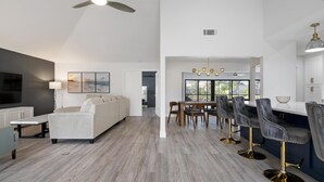 A modern kitchen with a dining area, featuring a bar with stools, a sofa, and a ceiling fan. - ⚓Luxury pool home with lakefront view just minutes from the beach!⚓ (Bradenton)