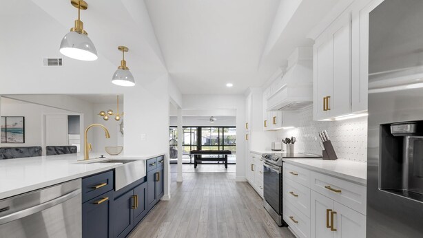 A modern kitchen with white cabinets, a stainless steel refrigerator, and a central island with a sink and gold fixtures. - ⚓Luxury pool home with lakefront view just minutes from the beach!⚓ (Bradenton)