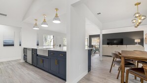 A modern kitchen with a central island, pendant lighting, and a dining area with wooden chairs. - ⚓Luxury pool home with lakefront view just minutes from the beach!⚓ (Bradenton)