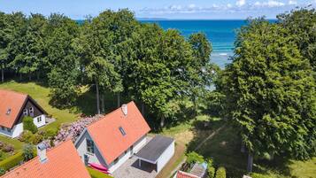 Et boligområde med huse med rødløbende tage, omgivet af frodige grønne træer, og udsigt til havet.
