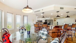 A modern kitchen with a central island, a dining area with a glass table, and a bar with stools.