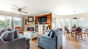 A spacious living room with a fireplace, a dining area with a table and chairs, and a large window offering a view of the outdoors.