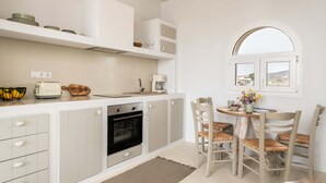 Una cocina moderna con armarios blancos, horno empotrado y una zona de comedor con sillas de mimbre y una mesa pequeña.